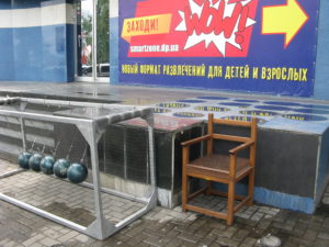 Sitting in front of the bowling alley is a chair with pointy stick like nails on it and this bowling ball game.